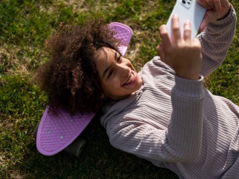 Mädchen aus Generation Alpha liegt auf dem Gras und schaut ins Handy